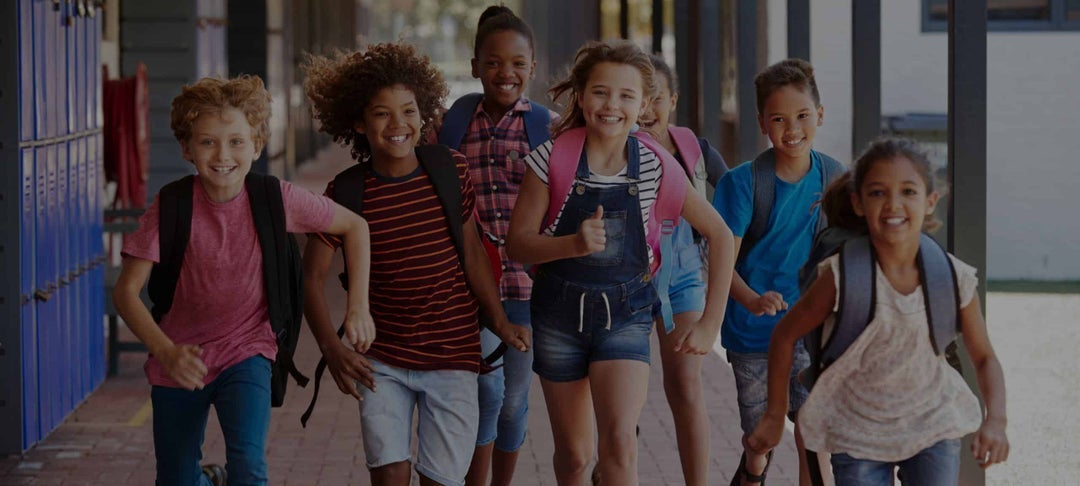 Elementary School students running down hall wearing backpacks